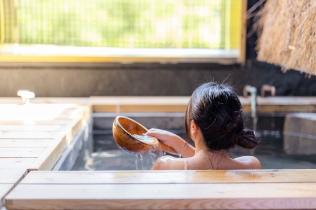 温泉に入りながらお湯を肩にかける後ろ姿の女性